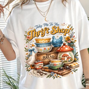 K&ouml;nnte beinhalten: Wei&szlig;es T-Shirt mit einem farbenfrohen Grafikdesign mit dem Text "Take Me To The Thrift Shop". Das Design umfasst Illustrationen von Schalen, einer Ente, Blumen und einer Brotkiste.