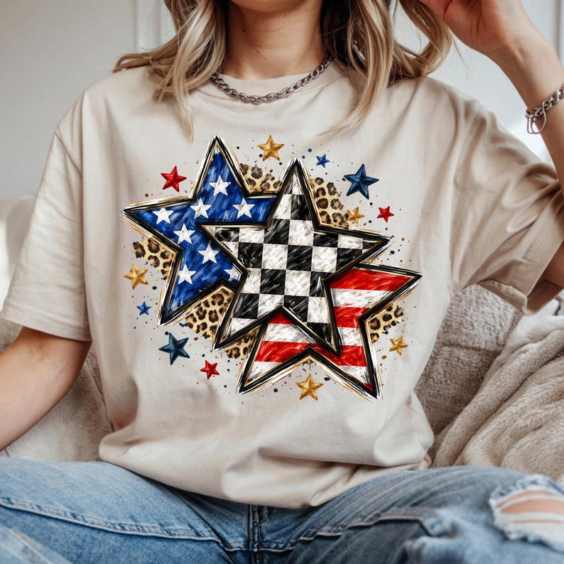 May include: Beige t-shirt featuring a patriotic star design. The design includes a blue star with white stars, a checkered star, and a red and white striped star. Additional gold and blue stars are scattered around the main design.