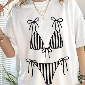 K&ouml;nnte beinhalten: Wei&szlig;es T-Shirt mit einem schwarz-wei&szlig; gestreiften Bikini-Design. Das Bikini-Oberteil und -Unterteil sind mit vertikalen Streifen und Schleifendetails versehen. Ein l&auml;ssiges Kleidungsst&uuml;ck f&uuml;r den Alltag.