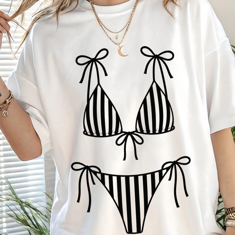 K&ouml;nnte beinhalten: Wei&szlig;es T-Shirt mit einem schwarz-wei&szlig; gestreiften Bikini-Design. Das Bikini-Oberteil und -Unterteil sind mit vertikalen Streifen und Schleifendetails versehen. Ein l&auml;ssiges Kleidungsst&uuml;ck f&uuml;r den Alltag.