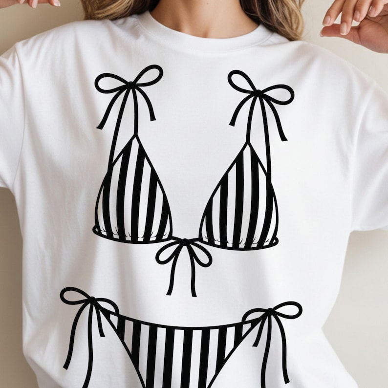 K&ouml;nnte beinhalten: Wei&szlig;es T-Shirt mit einer schwarz-wei&szlig;en Bikini-Grafik. Das Bikini-Oberteil und -Unterteil sind gestreift, mit Schleifen an den Tr&auml;gern und Seiten. Ein schlichtes, k&uuml;hnes Design, ideal f&uuml;r den Sommer.