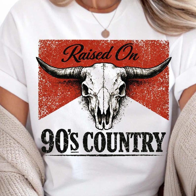 May include: White t-shirt featuring a graphic of a bull skull with long horns, set against a red and white background. The text "Raised On" is above the skull, and "90's COUNTRY" is below.