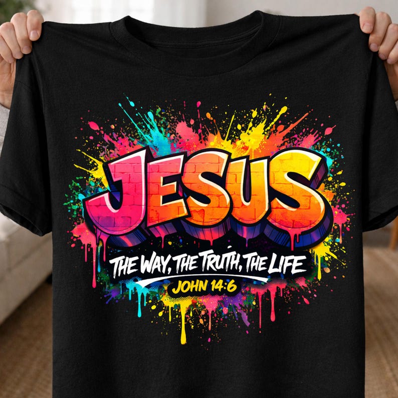 May include: Black t-shirt featuring the word "JESUS" in a graffiti-style design with vibrant colors. The shirt also includes the text "THE WAY, THE TRUTH, THE LIFE" and "JOHN 14:6".