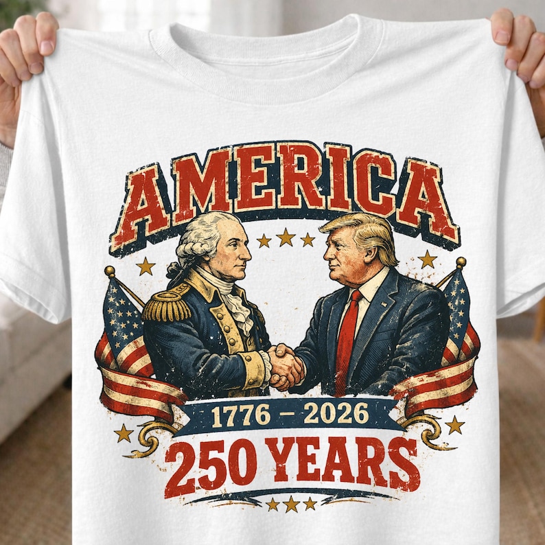 May include: White t-shirt featuring a graphic with the word "AMERICA" in red and blue. The graphic depicts two men shaking hands, with American flags and the text "1776-2026 250 YEARS".