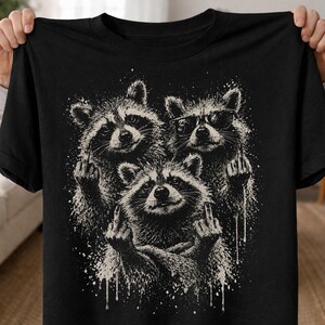 May include: Black t-shirt featuring a graphic of three raccoons. One raccoon wears sunglasses. All three raccoons are giving the middle finger. The graphic is in shades of white and gray with a splatter effect.