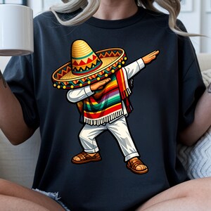 Pode incluir: Uma camiseta preta com uma ilustra&ccedil;&atilde;o de desenho animado de uma pessoa fazendo dab, usando um chap&eacute;u mexicano, uma serape colorida, cal&ccedil;as brancas e sand&aacute;lias marrons. O chap&eacute;u mexicano &eacute; amarelo com detalhes em vermelho, verde e amarelo. A serape &eacute; listrada.