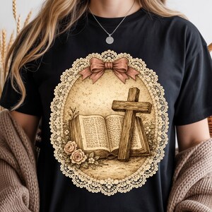 May include: Black t-shirt with a sepia-toned graphic of a cross, open book, and roses inside a lace-edged oval, topped with a brown bow. The design has a vintage, religious theme. The shirt is suitable for casual wear.
