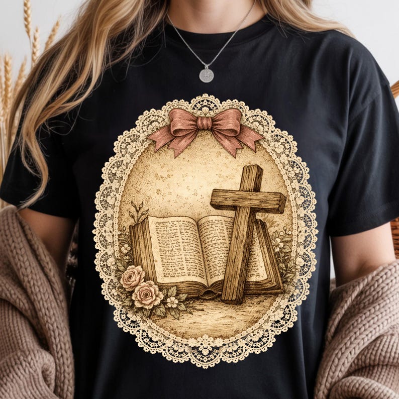 May include: Black t-shirt with a sepia-toned graphic of a cross, open book, and roses inside a lace-edged oval, topped with a brown bow. The design has a vintage, religious theme. The shirt is suitable for casual wear.