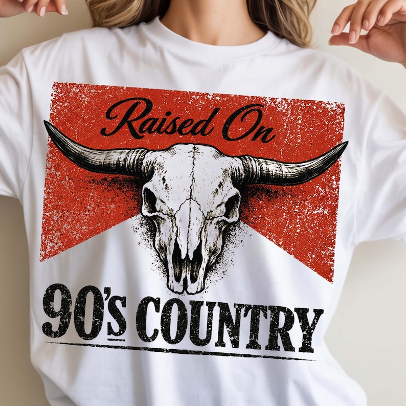 May include: White t-shirt featuring a bull skull graphic with long horns, set against a red, distressed background. The text "Raised On" is above the skull, and "90's COUNTRY" is below in a bold, black font.