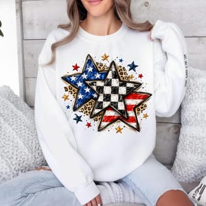 May include: White sweatshirt featuring a star design with American flag and checkered patterns. The stars are accented with leopard print and surrounded by smaller stars in red, blue, and gold. The sleeve has the text "STRONG. BRAVE. IT'S MY TIME."