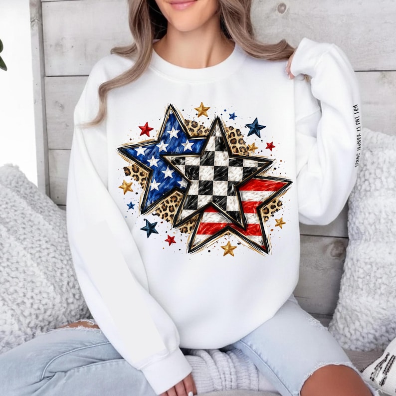 May include: White sweatshirt featuring a star design with American flag and checkered patterns. The stars are accented with leopard print and surrounded by smaller stars in red, blue, and gold. The sleeve has the text "STRONG. BRAVE. IT'S MY TIME."
