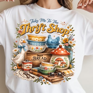 K&ouml;nnte beinhalten: Wei&szlig;es T-Shirt mit einer farbenfrohen Illustration. Das Design zeigt den Text "Take Me To The Thrift Shop", eine Ente, Schalen, eine Brotkiste, einen Pilztopf und Blumen. Das Design ist von Vintage inspiriert.