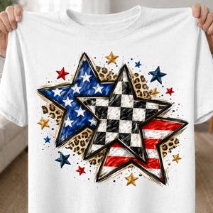 May include: White t-shirt featuring a star design with patriotic and racing themes. The design includes a blue star with white stars, a checkered flag star, and a red and white striped star, with leopard print accents and smaller stars.