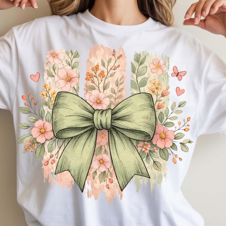 May include: White t-shirt with a green bow and floral design. The design includes pink flowers, green leaves, and a butterfly. The background has vertical stripes in shades of pink and green.