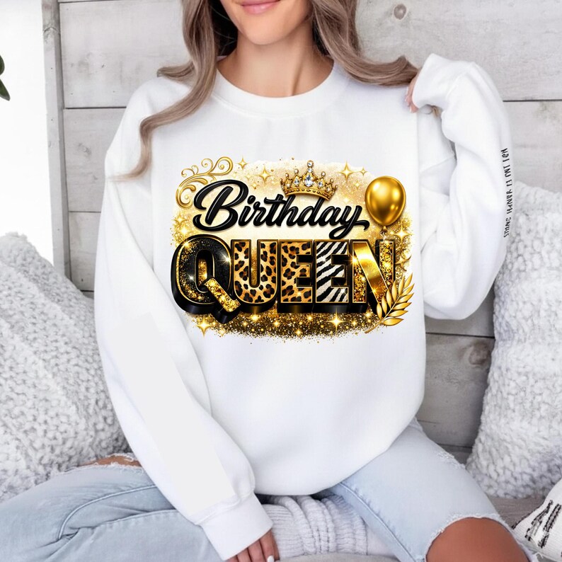 May include: White sweatshirt with a gold and black "Birthday Queen" graphic. The graphic includes a crown, balloon, and leopard print accents. The sweatshirt is a long-sleeved crew neck.