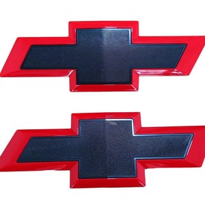 May include: Two red and black Chevrolet bow tie emblems. The emblems have a glossy red outline and a textured black center. The iconic logo is displayed against a white background.