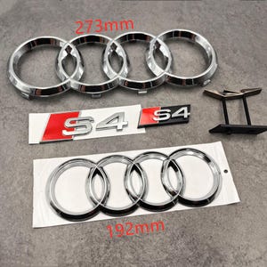 May include: Chrome car emblems and badges. The image shows two sets of four interlocking rings, one set measuring 273mm and the other 192mm. Also included are two "S4" badges with red accents and a black mounting bracket.