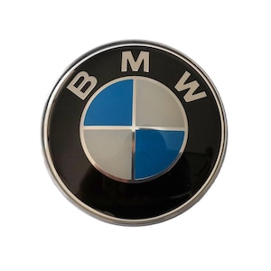 May include: A round, black BMW emblem with a silver border. The emblem features the BMW logo, a circular design divided into four quadrants: blue, white, and silver. The letters "B", "M", and "W" are in silver.