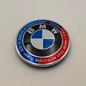 May include: A circular BMW emblem with a black background and a blue and white center. The emblem has the text "NOT JUST A DREAM M POWER BMW PERFORMANCE I KNOW THAT MY FUTURE IS" in white lettering.