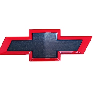 May include: A red and black Chevrolet emblem, featuring the iconic bowtie shape. The emblem has a glossy red border and a textured black center, set against a white background. This automotive accessory is designed for vehicle customization.