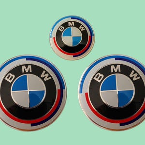 May include: Three BMW emblem stickers. The stickers feature the BMW logo in a circular design with a blue, white, and black colour scheme. The largest stickers have a diameter of approximately 7.6 cm.