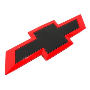 May include: A red and black Chevrolet emblem, a stylized bow tie shape. The emblem has a glossy red border and a textured black center, set against a white background. This automotive accessory is a classic car part.