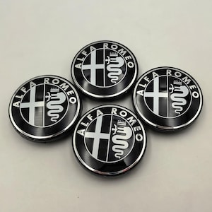以下が含まれることがあります： 黒とシルバーのアルファロメオのホイールセンターキャップ4個セット。各キャップには、アルファロメオのロゴ、白い十字と蛇、ブランド名が円形パターンで表示されています。