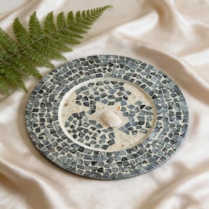 Könnte beinhalten: Eine weiße Keramik-Tasse mit schwarzem Henkel und dem Text "But First, Coffee" in fetter, schwarzer Schrift. Die Tasse steht vor einem verschwommenen Hintergrund, der ihr schlichtes Design hervorhebt.