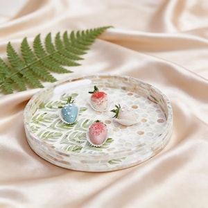 May include: A round decorative tray with a mosaic border holds four chocolate-covered strawberries. The strawberries are coated in blue, pink, and white chocolate, and decorated with sprinkles. A green fern leaf is in the background.