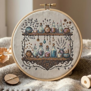May include: Cross-stitch embroidery of a shelf with various potion bottles in a wooden embroidery hoop. The bottles are in shades of blue, brown, and purple. The background is a neutral linen fabric. The embroidery hoop is made of wood.