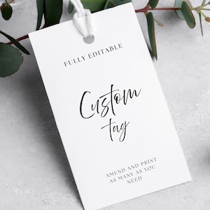Peut inclure: Une étiquette personnalisée rectangulaire blanche avec une ficelle, avec les mots "FULLY EDITABLE", "Custom Tag", et "AMEND AND PRINT AS MANY AS YOU NEED" en noir. L'étiquette est posée sur un fond gris clair avec du feuillage vert.