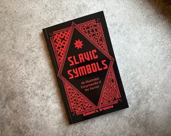 May include: A black book titled "SLAVIC SYMBOLS" with red geometric designs and text. The book cover features a red star and the subtitle "An Illustrated Encyclopedia of the Sacred". The author's name, Radomira Gromova, is also visible.