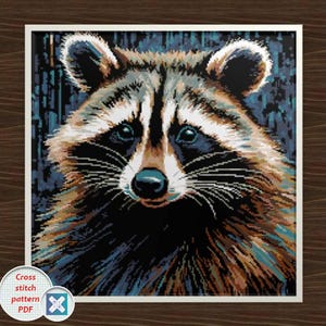 May include: A framed cross-stitch pattern featuring a detailed raccoon portrait. The raccoon has brown and black fur, with a white face and dark eyes. The background is a dark blue, and the text "Cross stitch pattern PDF" is visible.