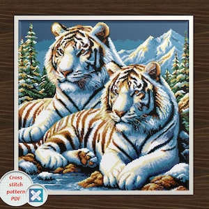 Peut inclure: Motif de point de croix encadré représentant deux tigres blancs aux rayures marron, sur fond de montagnes enneigées et de sapins. Les tigres sont couchés, avec une expression sereine. La palette de couleurs comprend des nuances de blanc, de marron, de bleu et de vert.