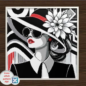 Può includere: Schema punto croce PDF di una donna con cappello e occhiali da sole. L'immagine è un design grafico in bianco, nero e rosso. La donna indossa un grande cappello con una fascia rossa e un fiore bianco. L'immagine è incorniciata.