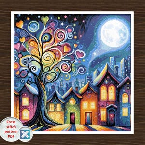 Op de afbeelding: Een kleurrijk kruissteekpatroon dat een grillige nachtscène uitbeeldt. Een grote boom met hartvormige bladeren en wervelende takken staat voor een rij huizen. Een volle maan en een sterrenhemel completeren het fantasielandschap. De tekst "Cross stitch pattern PDF" is inbegrepen.