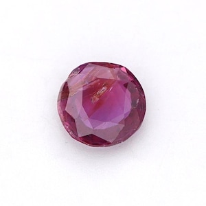 Puede incluir: Una gema redonda y facetada de un tono magenta intenso. La gema se encuentra sobre un fondo blanco, mostrando sus superficies pulidas y su claridad interna. La forma de la gema es un círculo perfecto.