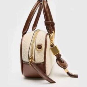 May include: A small, rectangular handbag with a cream-coloured woven body and brown leather trim. It features a gold zip, a short handle, and a detachable shoulder strap. The bag has a structured design and a minimalist aesthetic.