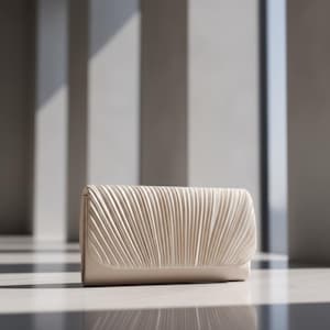 Peut inclure: Une pochette crème avec un design plissé sur le rabat avant. Le sac rectangulaire a une finition lisse et mate et un style simple et élégant. L'arrière-plan présente un cadre architectural moderne avec de la lumière et de l'ombre.