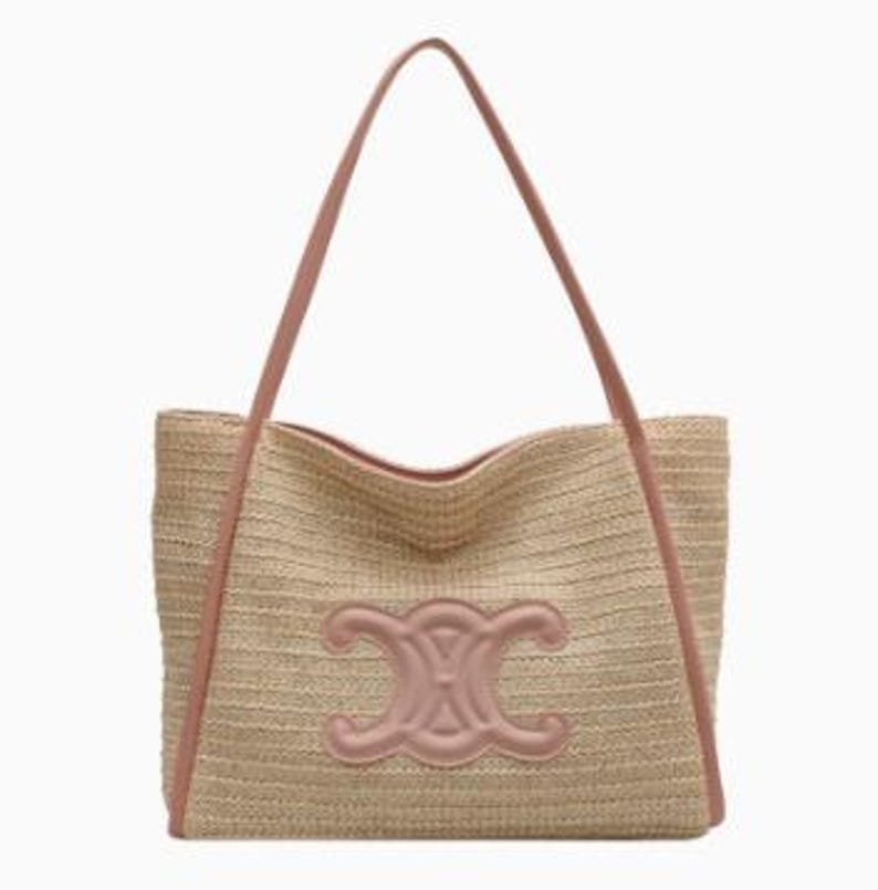 May include: A beige woven tote bag with a pink leather trim and handles. The bag features a large pink emblem on the front. The tote bag is designed with a rectangular shape and a spacious interior, perfect for carrying essentials.