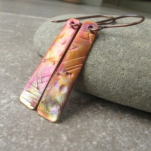 May include: A pair of copper earrings with a hammered texture and a rainbow iridescent finish. The earrings are long and rectangular in shape.