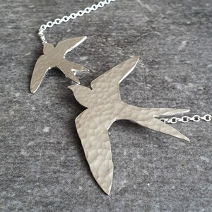 Peut inclure: Un collier en argent avec deux pendentifs en forme d'oiseau en argent martel&eacute;. Les oiseaux sont orient&eacute;s dans la m&ecirc;me direction et sont reli&eacute;s par une cha&icirc;ne en argent.