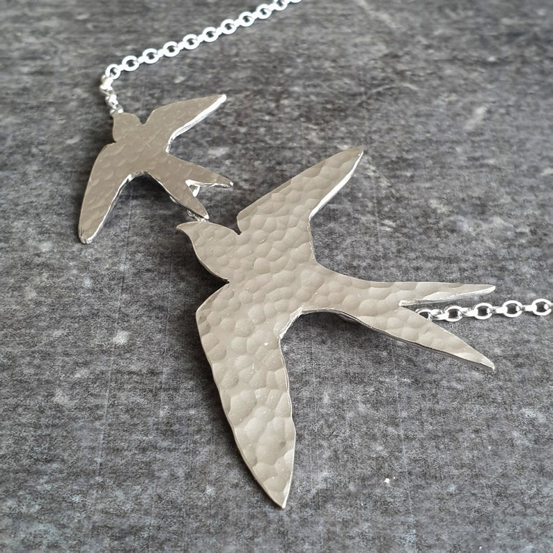 Peut inclure: Un collier en argent avec deux pendentifs en forme d'oiseau en argent martel&eacute;. Les oiseaux sont orient&eacute;s dans la m&ecirc;me direction et sont reli&eacute;s par une cha&icirc;ne en argent.