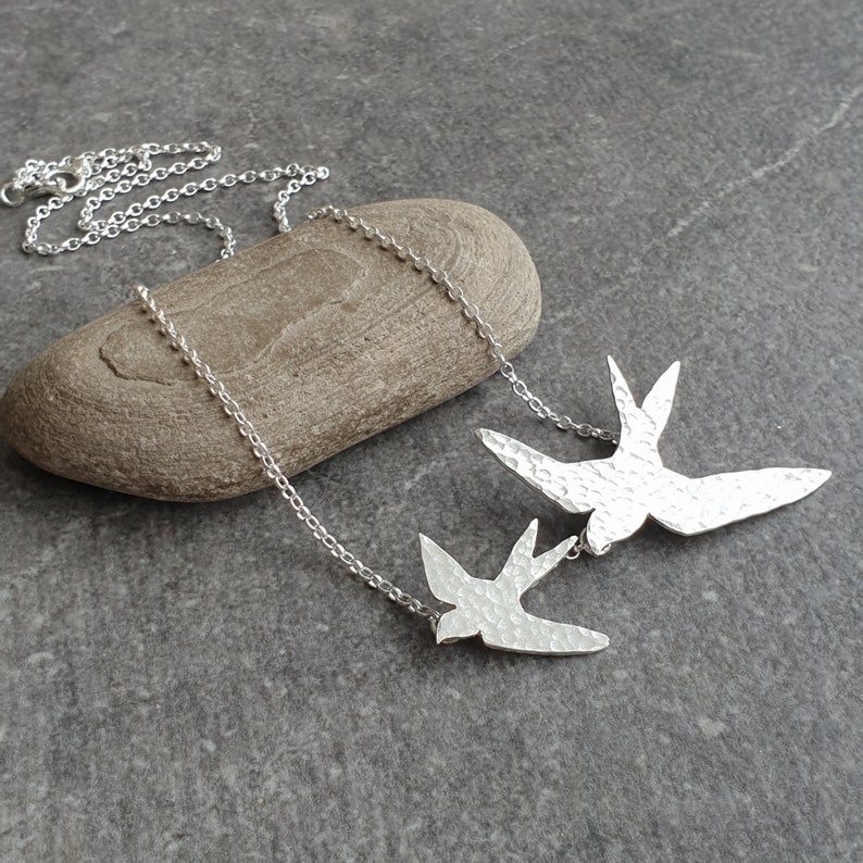 Peut inclure: Un collier en argent avec deux pendentifs en forme d'oiseau en argent martel&eacute; textur&eacute;. Le plus grand oiseau vole au-dessus du plus petit.