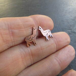 Könnte beinhalten: Ein Paar Kupfer-Lama-Ohrstecker. Die Ohrringe sind klein und zart und haben ein schlichtes, stilisiertes Design eines Lamas.