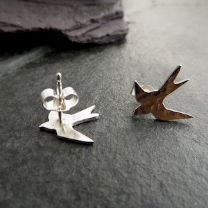 Op de afbeelding: Een paar zilveren zwaluw oorbel studs. De oorbellen zijn gemaakt van gehamerd metaal en hebben een eenvoudig, elegant ontwerp.
