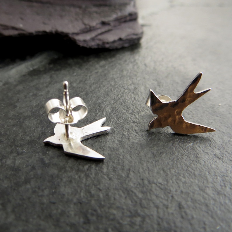 Op de afbeelding: Een paar zilveren zwaluw oorbel studs. De oorbellen zijn gemaakt van gehamerd metaal en hebben een eenvoudig, elegant ontwerp.