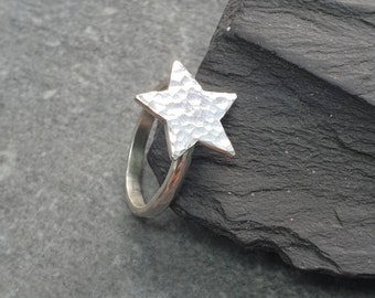 May include: A silver ring with a textured star-shaped design. The ring is on a gray background.