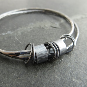 May include: A silver bangle bracelet with a textured finish and a cluster of smaller rings attached to the centre. The bracelet is made of multiple strands of wire.