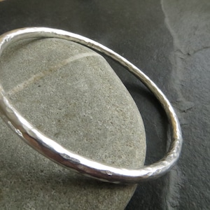 May include: A silver bangle bracelet with a hammered finish. The bracelet is thick and has a rounded shape.